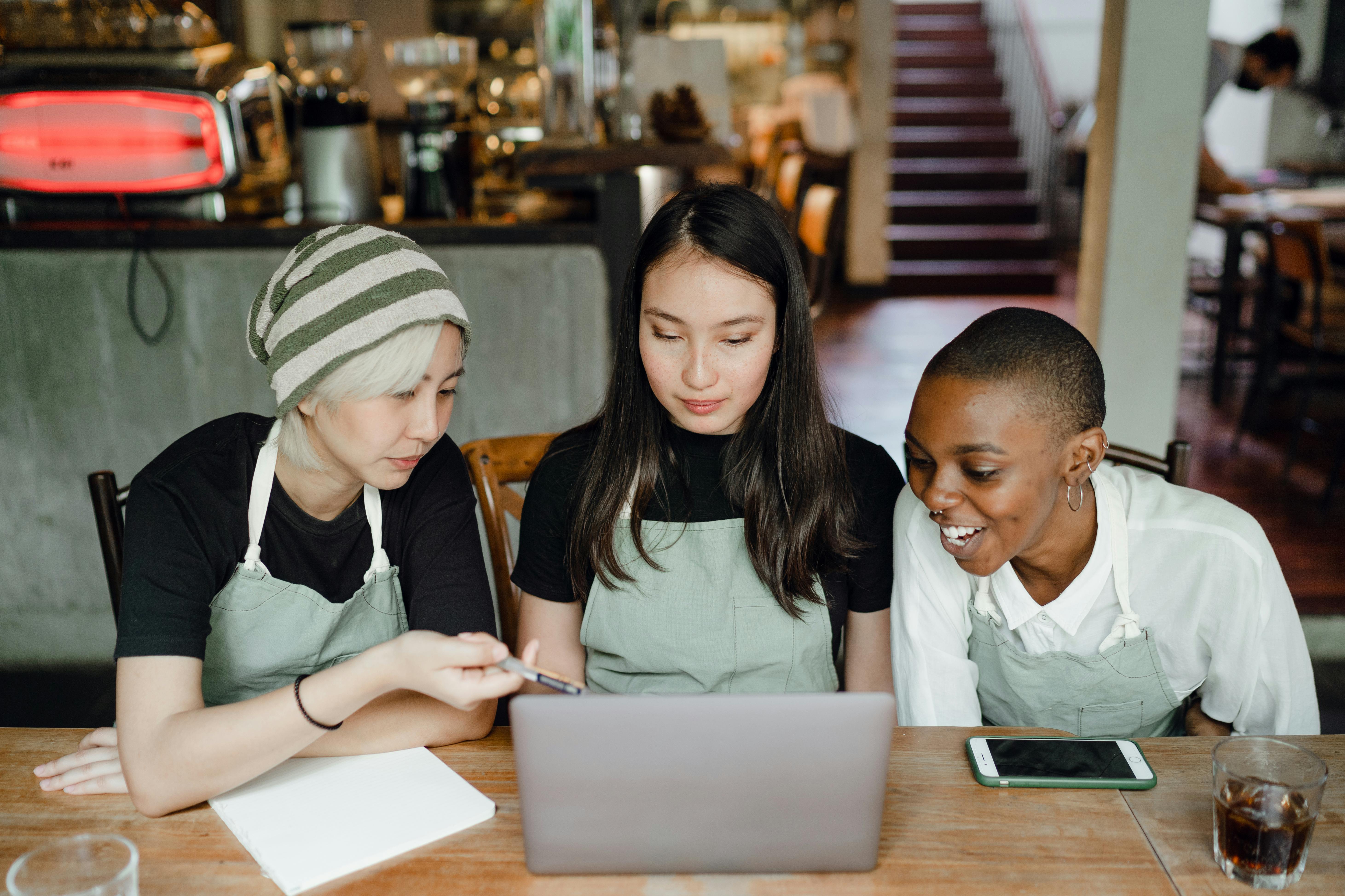 Three coffee shop business partners looking at a laptop, ensuring business good standing with a registered agent.