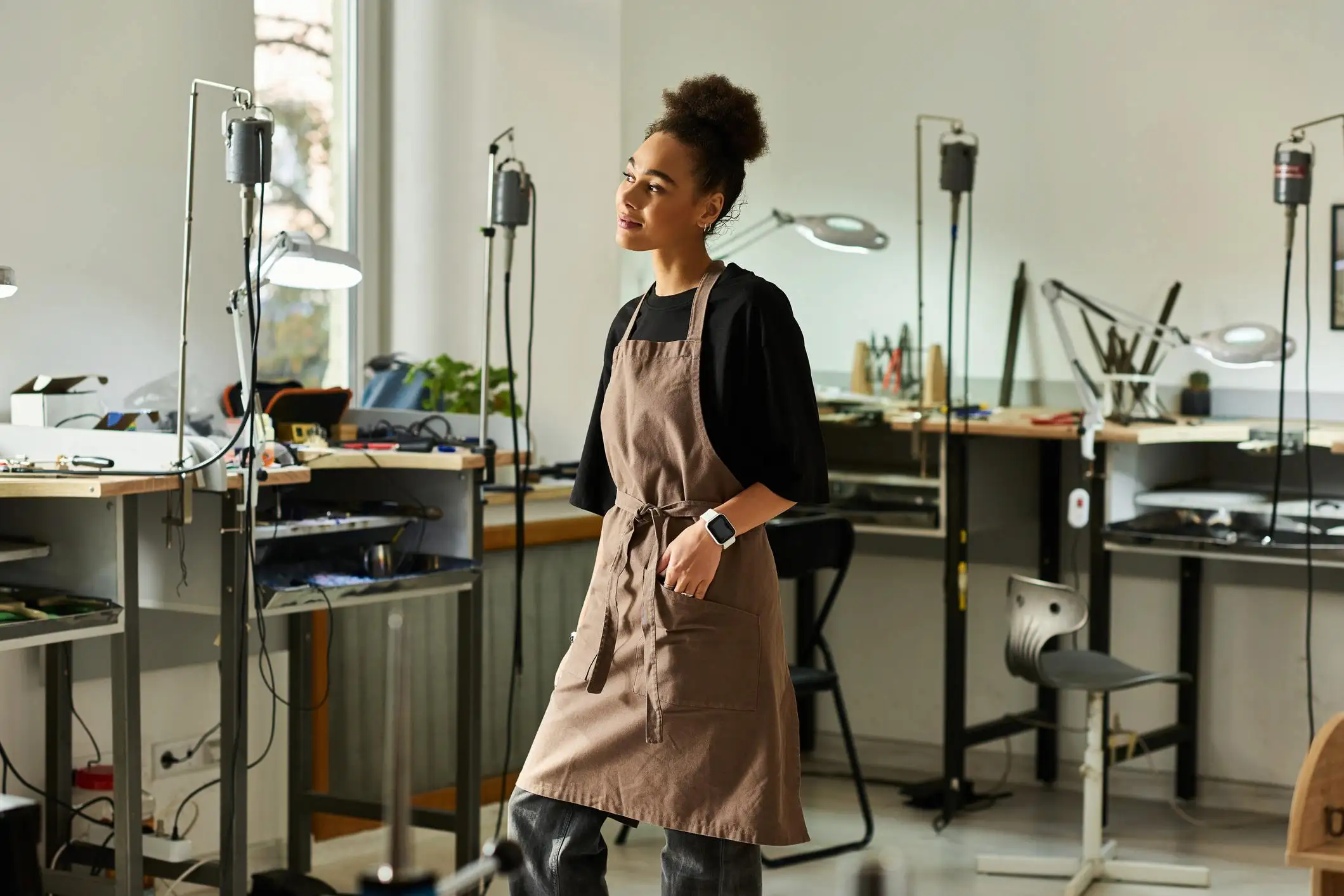 Thoughtful woman in an apron standing in her jewelry workshop, preparing to foreign qualify LLC.