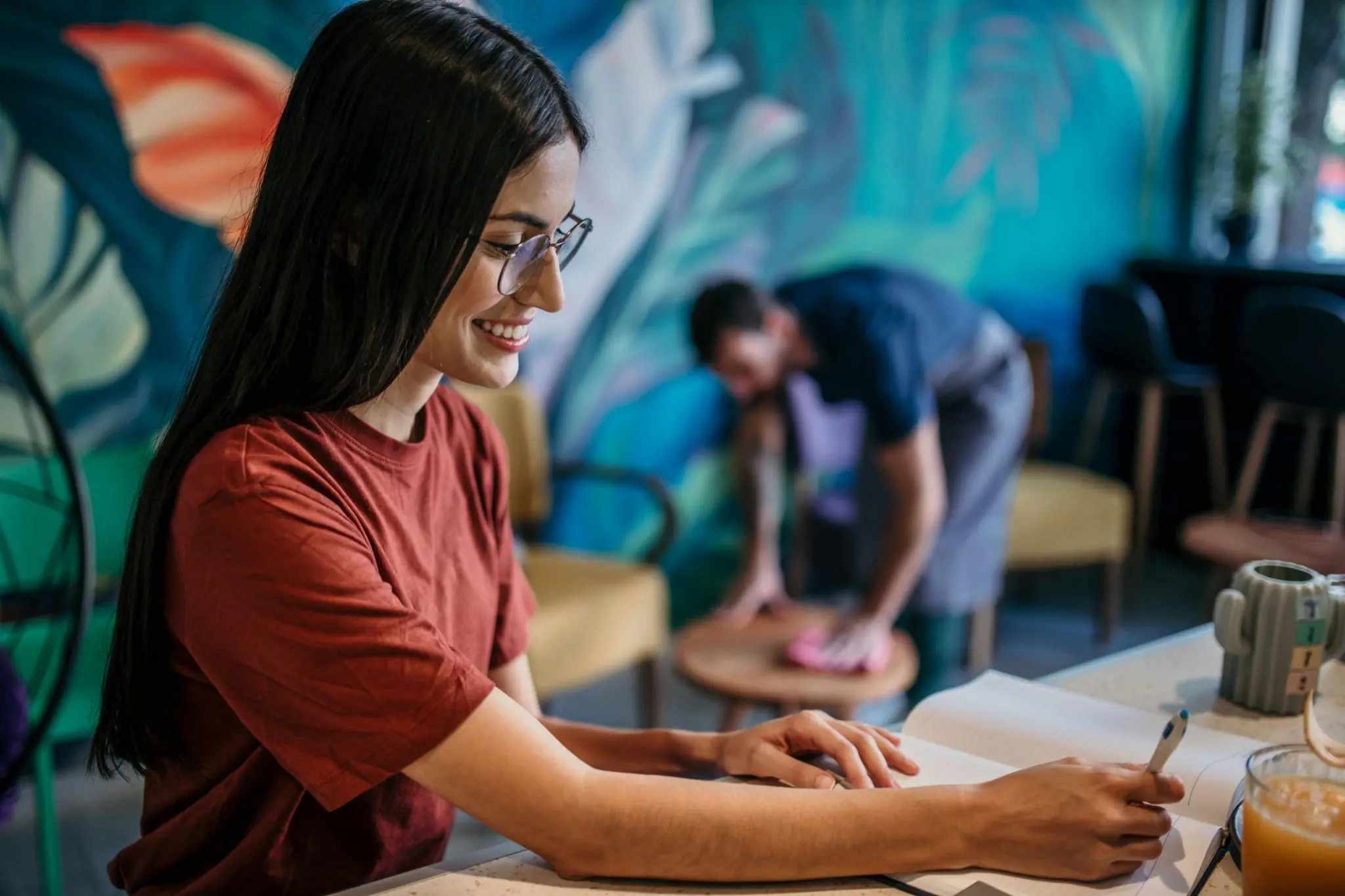 Smiling cafe owner taking notes on a DBA vs LLC while an employee cleans in the background.