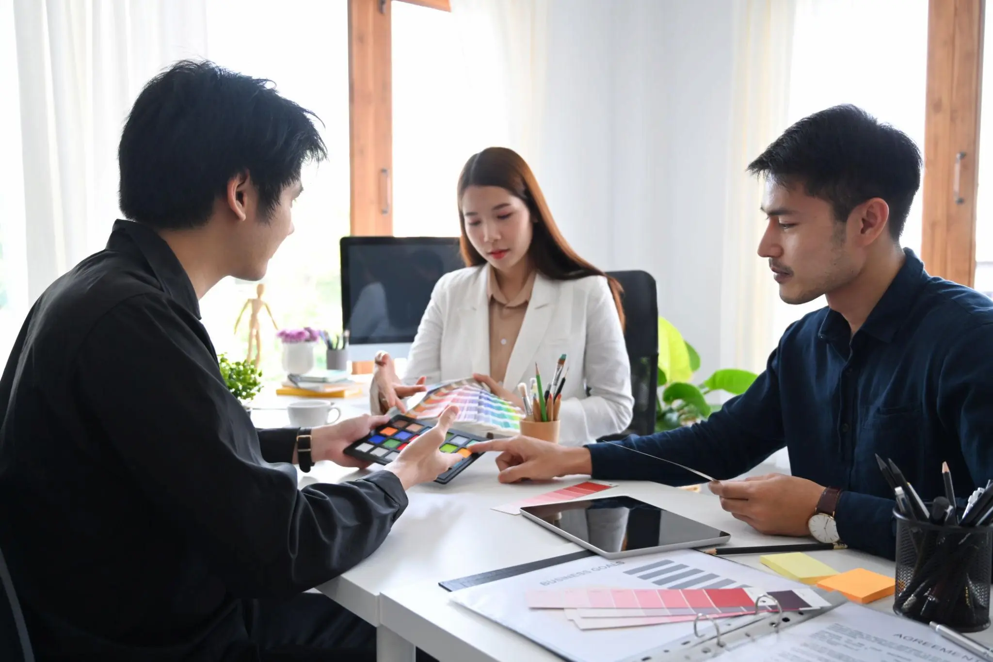 Graphic designers and a client reviewing color swatches and business goals at an office desk.