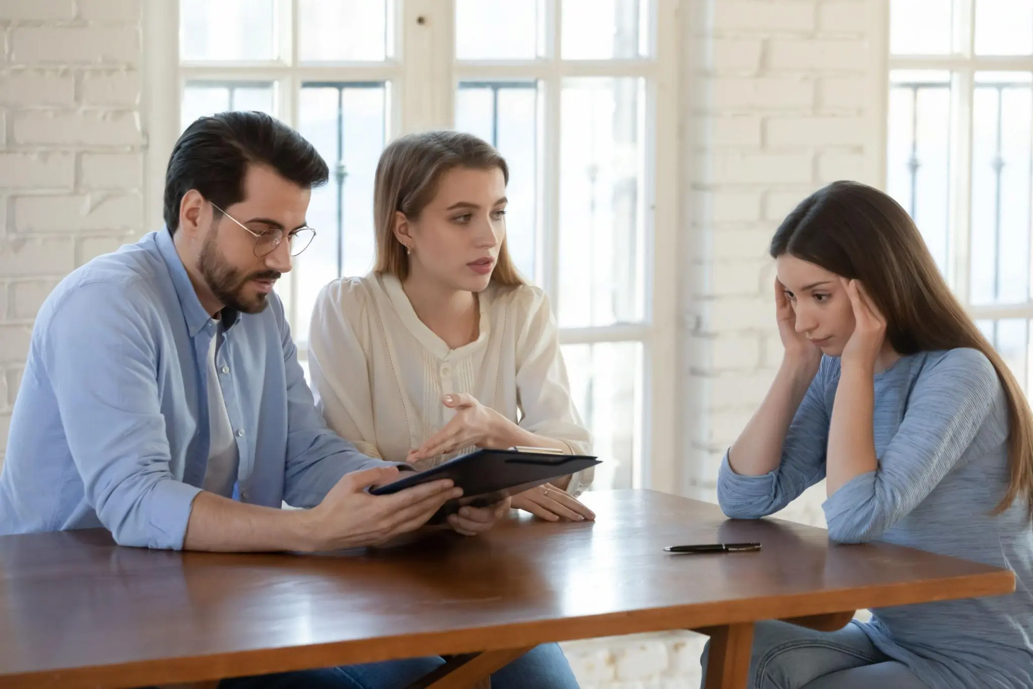Stressed woman holding her head as colleagues review an annual report to reinstate a Florida corporation.
